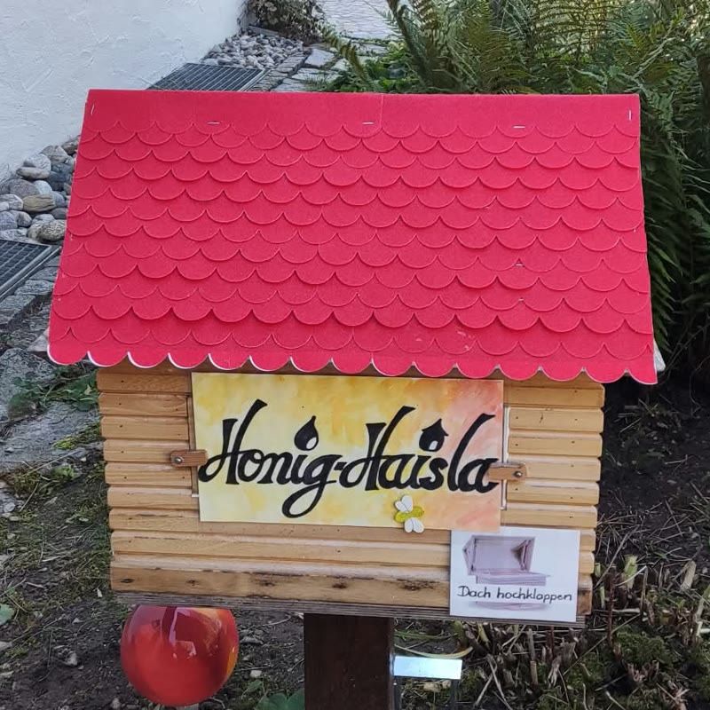 Das Haisla von vorn: rotes Schindeldach, Schild Honig-Haisla, daneben der Zettel Dach hochklappen.